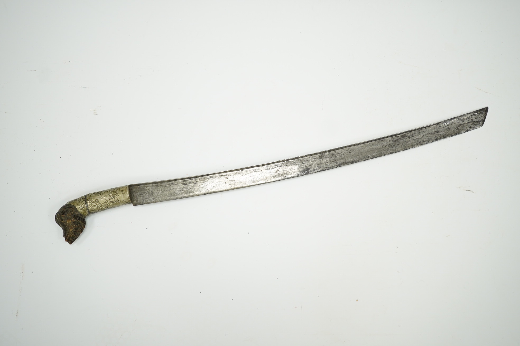 A Malaysian sword Parang, with broad curved pattern welded single edged blade, carved horn pommel, and embossed nickel mounts, in its wooden scabbard. Condition - good